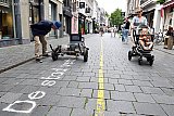 26-06-2022 Breda - Een voorbijganger kijkt naar Zandschrijver SKRYF deze schreef in de binnenstad teksten op straat tijdens de cultuurzondag. Hier schrijft de rijdende printer: -De stad verbleef eeuwenlang dichtbij- in De Veemarktstraat. - Fotokrant