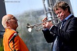 18-05-2023 Breda - Een in oranje gehulde dirigent kijkt tevreden met een schuin oog  naar een trompet spelende Jazzmuzikant. - Fotokrant